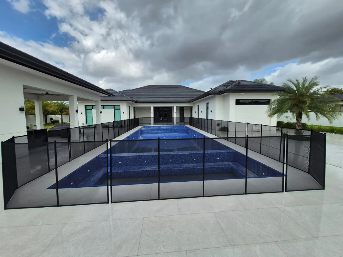 Black mesh fence around a rectangular blue swimming pool beside a covered terrace in Miami Beach
